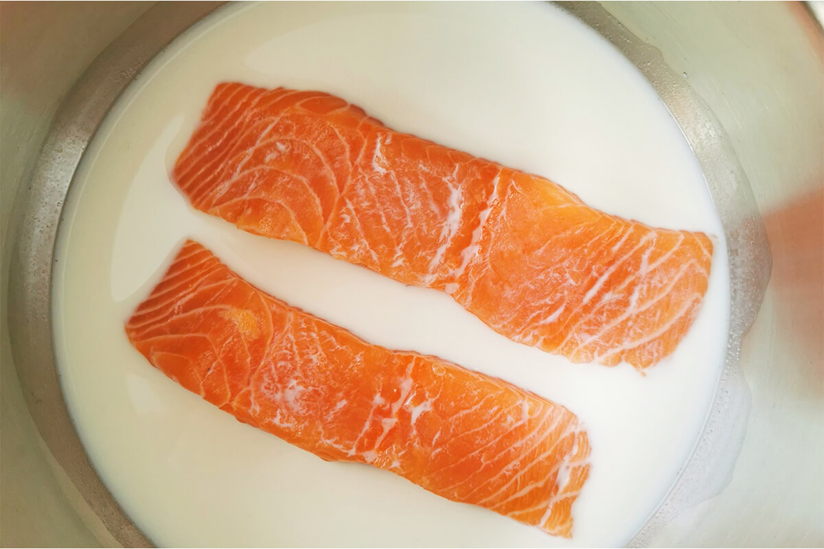 Two salmon fillets in a saucepan of milk