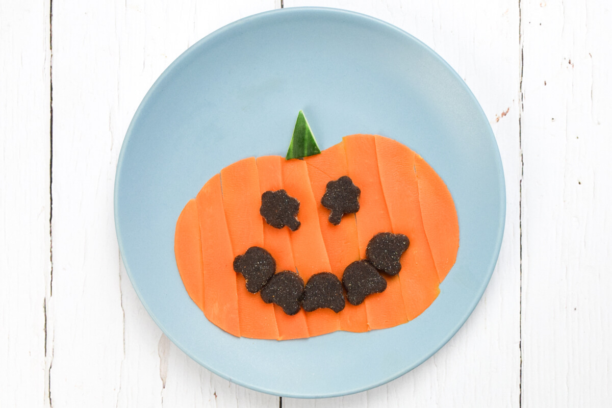 Blue plate with a pumpkin shape made of steamed carrot, and Organix Pic-Nix for eyes and mouth.