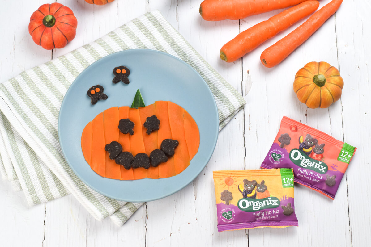 Blue plate with a pumpkin shape made of steamed carrot, and Organix Pic-Nix for eyes and mouth.