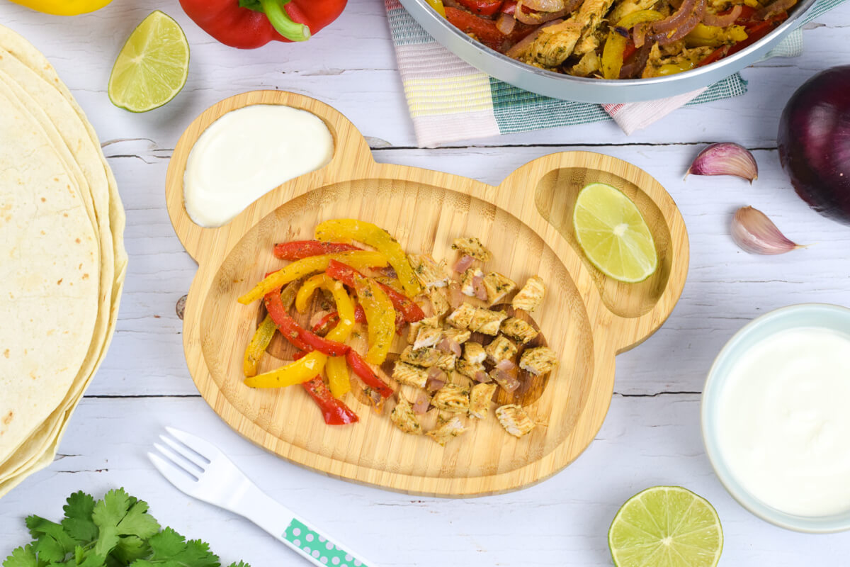 A serving of chicken and pepper fajitas with sour cream and a lime wedge