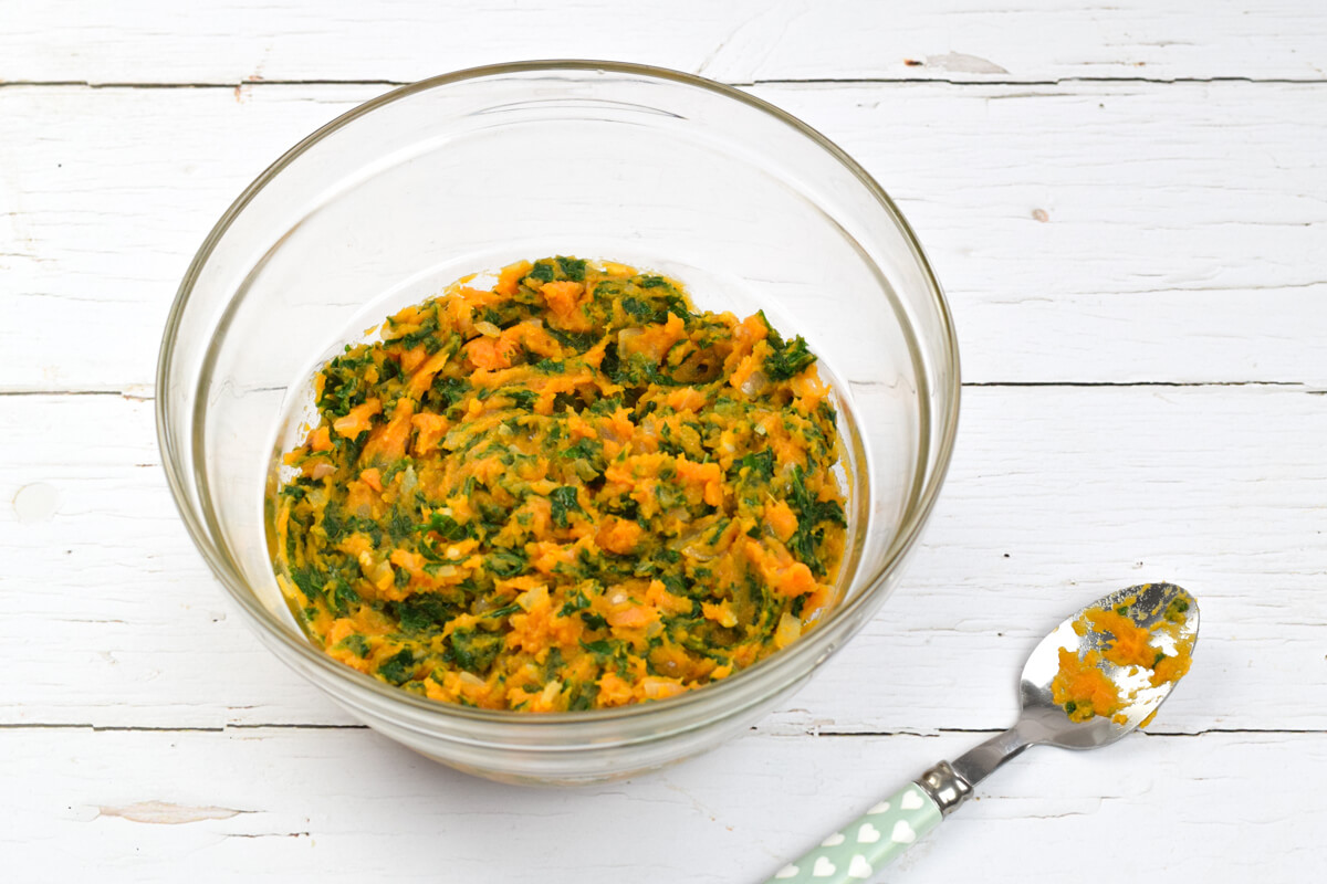 A glass bowl with mashed sweet potato, kale, fried onion and garlic